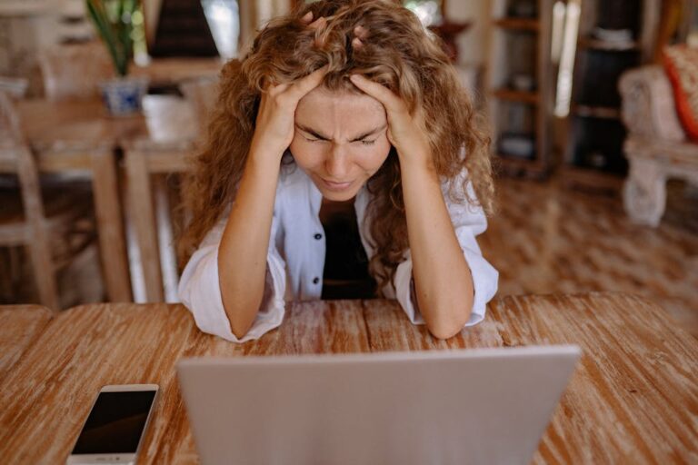 Distressed woman sitting at a desk while looking at a laptop